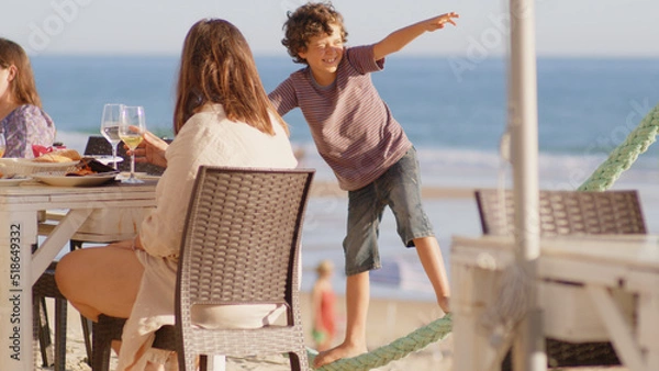 Fototapeta 4 sibling boys look at the camera smiling, play while running through a restaurant in front of the camera, eat ice cream, hug their mother