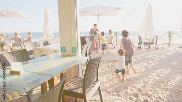 Fototapeta 4 sibling boys look at the camera smiling, play while running through a restaurant in front of the camera, eat ice cream, hug their mother