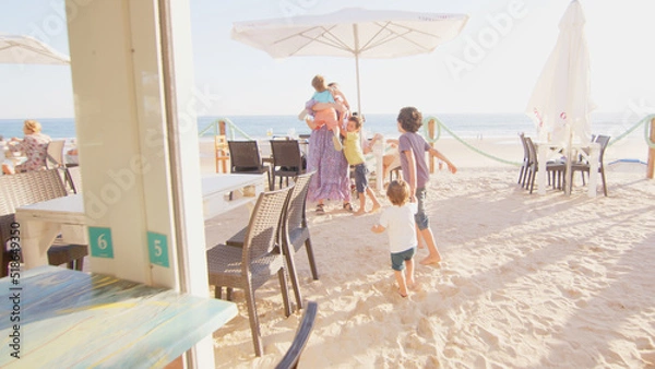 Fototapeta 4 sibling boys look at the camera smiling, play while running through a restaurant in front of the camera, eat ice cream, hug their mother