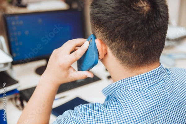 Obraz a young Asian businessman is talking on the phone to discuss work in the office. the man is Asian.