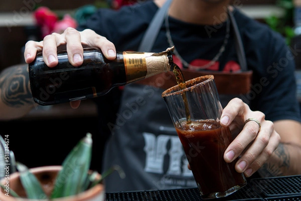 Fototapeta Hands of a latin guy working as a bartender pouring a beer to prepare a cocktail drink in a bar. Barman preparing an alcoholic drink in a glass.