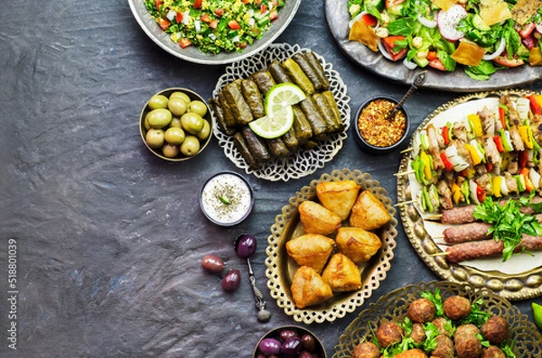 Fototapeta Arabic cuisine;Assorted of middle eastern traditional dishes. Stuffed vine leaves,olives, kibbeh, shish tawook, flafel, sambusak, tabbouleh and fattoush salad. Halal food. Top view with copy space.