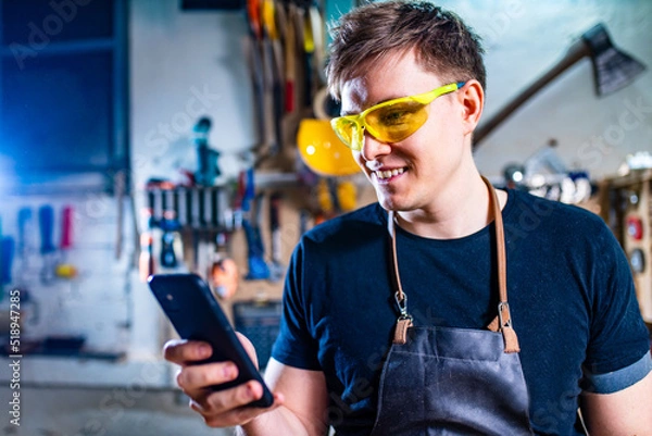 Fototapeta Portrait of handsome carpenter looking at he smartphone in workshop