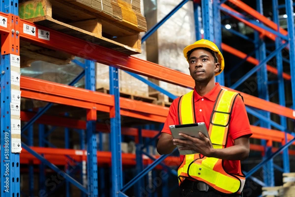 Fototapeta A man in charge of a large warehouse is checking the number of items in the warehouse that he is responsible for. By tablet