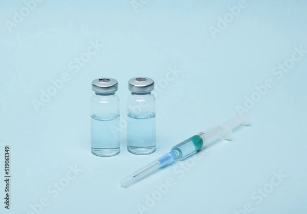 Fototapeta Syringe with two vials of vaccine liquid on a blue background