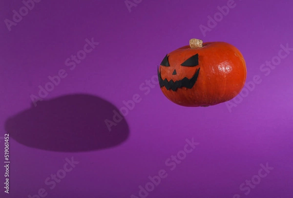 Fototapeta Floating halloween pumpkin with scary face on purple background with shadow