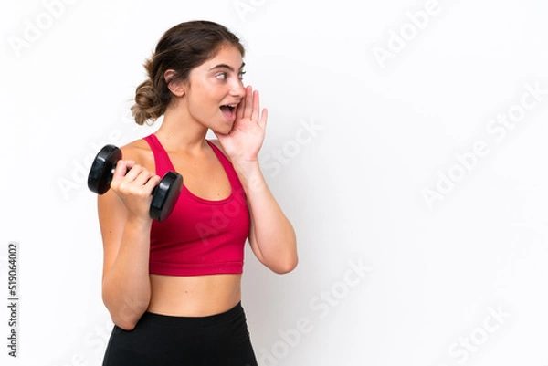 Obraz Young sport caucasian woman making weightlifting isolated on white background shouting with mouth wide open to the side