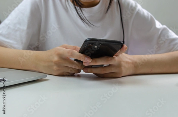Fototapeta Young girl hand holding mobile smartphone communication and digital internet social network technology on table.