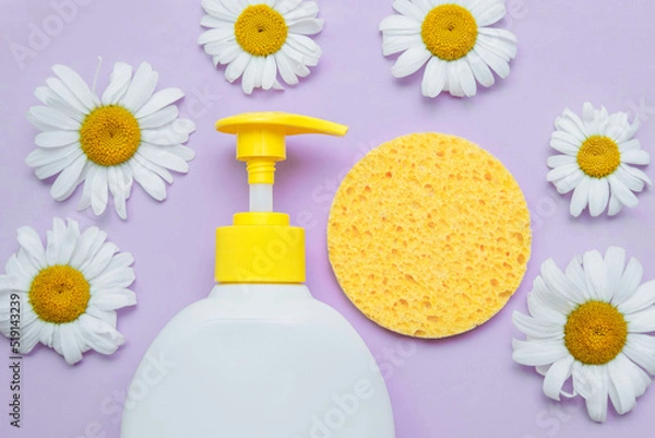 Fototapeta Plastic cosmetic white bottle with yellow dispenser and sponge, chamomile flowers close-up with empty space for text, conscious space, on purple background, flat lay,  concept of skin, face, body care