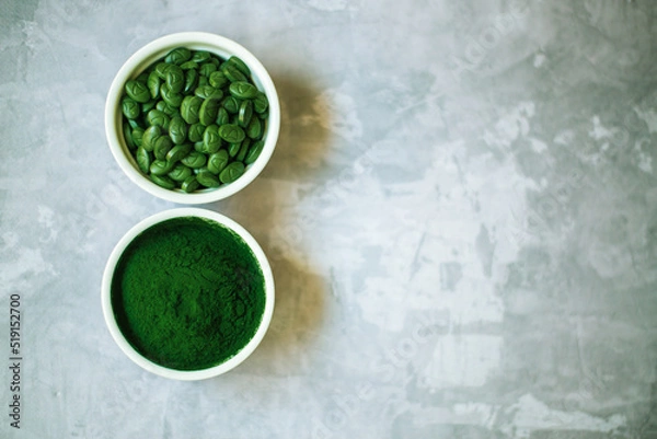 Fototapeta spirulina powder and tablets in white plates on concrete background