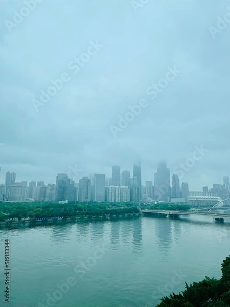 Fototapeta Downtown in Clouds. Skyscraper hidden in Foggy Clouds. City Skyline with River and Bridge