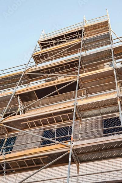 Fototapeta Scaffolding on the faсade of the building under construction. A vertical image.