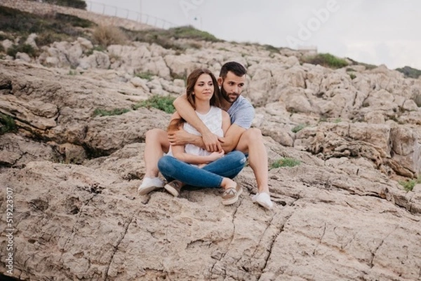 Obraz A man is holding his girlfriend while both are sitting on the rocks in Spain