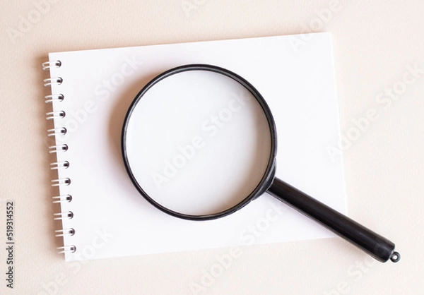Fototapeta The magnifying glass lies on the notebook on a white page.