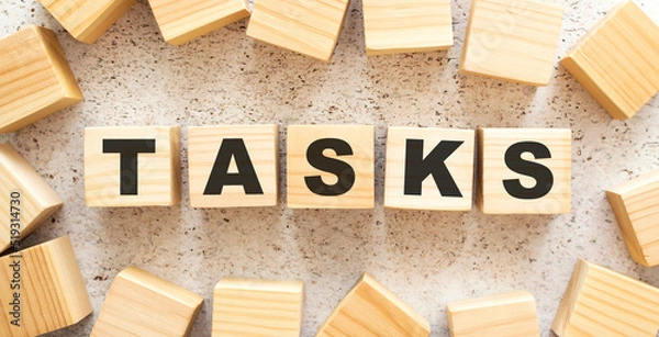 Fototapeta The word TASKS consists of wooden cubes with letters, top view on a light background.