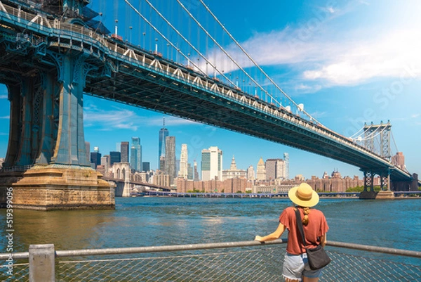 Fototapeta Young woman enjoying view of city skyline in New York. Happy lifestyle girl with hat traveling tourist on bridges.