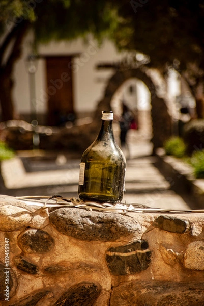 Obraz Vertical format photograph of a bottle of green wine without content on a small white wall in a square in the town of Cachi, Salta, Argentina.
