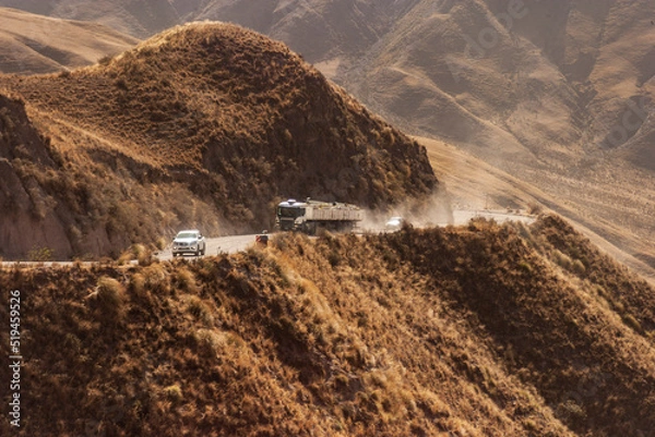 Obraz Winding dirt road between the mountains with vehicles circulating on it