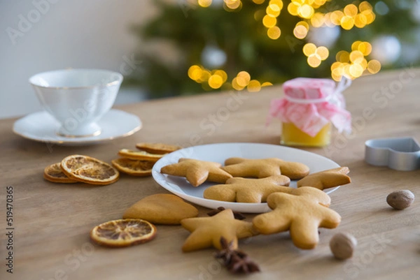 Fototapeta Plate with traditional ginger cookies in front of a Christmas tree with a herald of lights. 