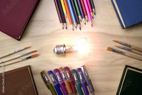 Obraz fountain pens pencils brushes books and a burning light symbolizing knowledge on the table concept education science