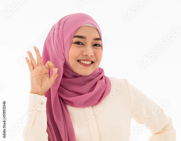 Fototapeta Beautiful and smiling young muslim woman presenting OK hand gesture or hand signal isolated on white background. Concept of confirmaing sign, surely signal