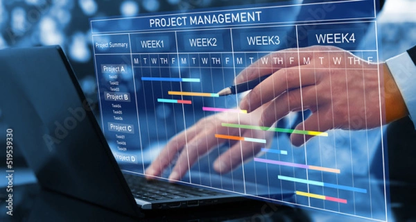 Fototapeta Project manager working on laptop and updating tasks and milestones progress planning with Gantt chart scheduling interface for company on virtual screen. Business Project Management System.