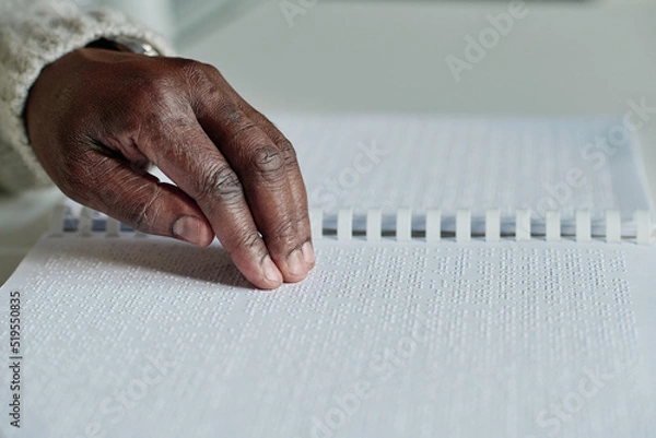 Fototapeta Close-up of senior blind man reading braille in opened book at table