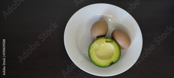 Fototapeta Boiled Eggs and Avocado in a white plate placed on a black wooden table top view