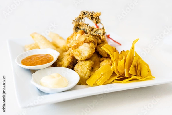 Fototapeta Peruvian food: chicharron de pescado or fish cracklings with fried cassava and onion salad with chili, served on a white plate. White background