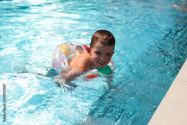 Fototapeta A little boy swims in a beautiful blue pool in an inflatable circle.