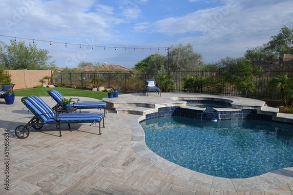 Fototapeta A desert landscaped backyard in Arizona featuring a travertine tiled pool deck.