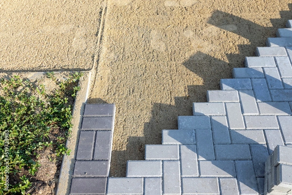Fototapeta Paving the road from garden bricks by a professional paver. Laying gray concrete paving slabs on a gravel and sand base.