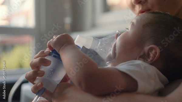 Obraz Side view of baby breathing an inhaler at home