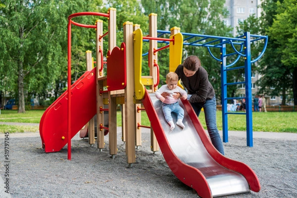 Fototapeta Young mother playing with her baby on the playground.
