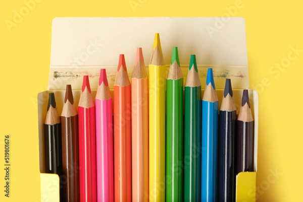Fototapeta Multicolored pencils in a box isolated on yellow.