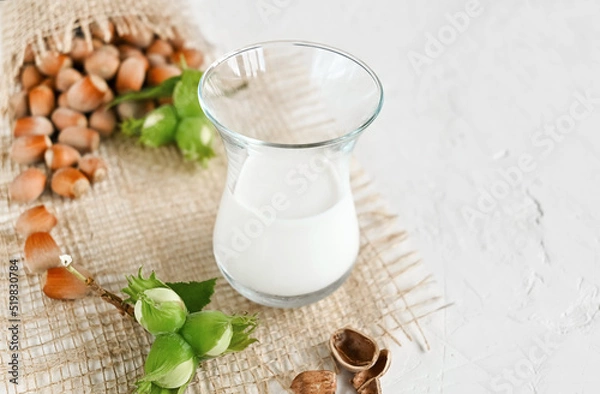 Fototapeta Hazelnut non dairy milk in a glass and hazelnuts on a burlap, copy space. 