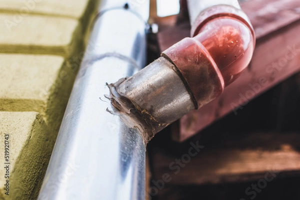Fototapeta Maintenance of a rain gutter. Professional paste to repair cracks in the drainage pipe of a residential building. Junction of a water duct on the exterior wall of a home