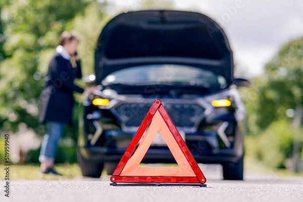 Fototapeta Red emergency stop sign and woman talking on the phone near a broken car on the road