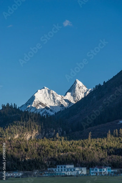 Fototapeta The houses cling to the hillside and snow-capped mountain peaks
