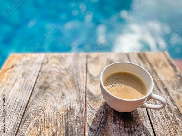 Obraz Cup of coffee on brown wooden table with defocus swimming pool or gradient blue blurry background