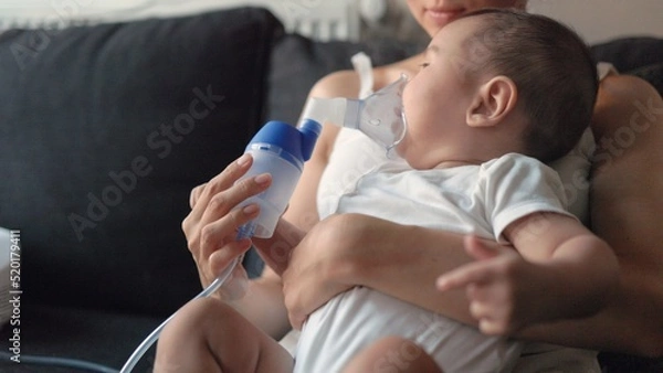Obraz Side view of baby breathing an inhaler at home