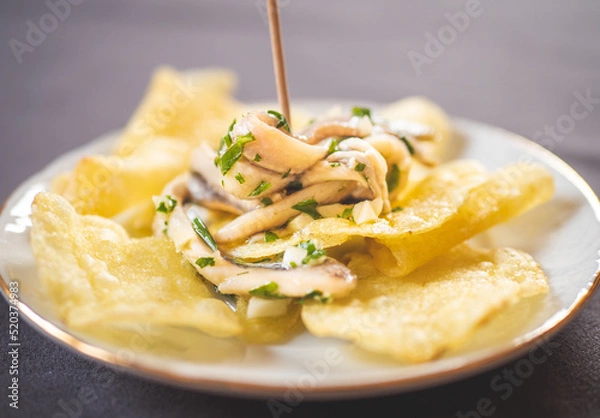 Fototapeta Potato chips with pickled anchovies in a white round plate on a table. Typical Spanish food called “tapa” to eat in a bar.