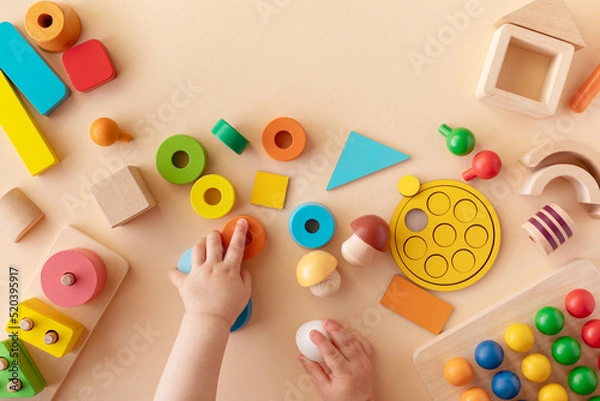 Fototapeta Toddler activity for motor and sensory development. Baby hands with colorful wooden toys on table from above.