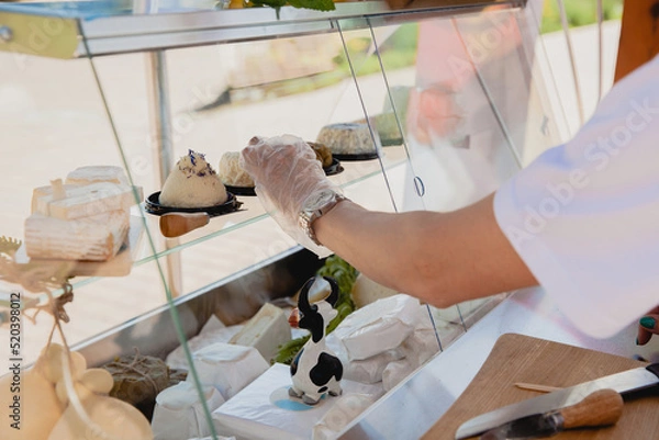Obraz a seller in plastic gloves lays out homemade cheese on a glass counter at a street fair in the summer