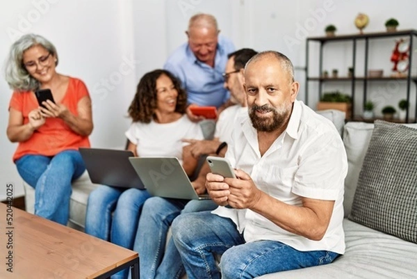 Fototapeta Group of middle age friends using laptop and smartphone sitting on the sofa at home.
