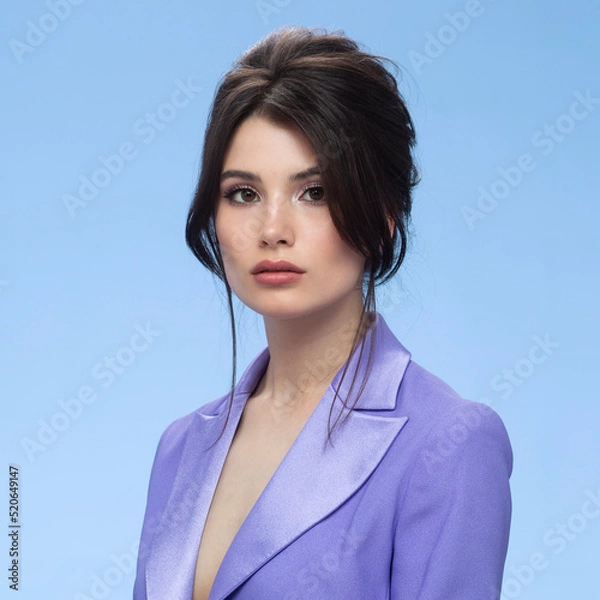 Fototapeta Front image of a young woman in a stylish purple suit in attractive, looking at camera, isolated blue background.