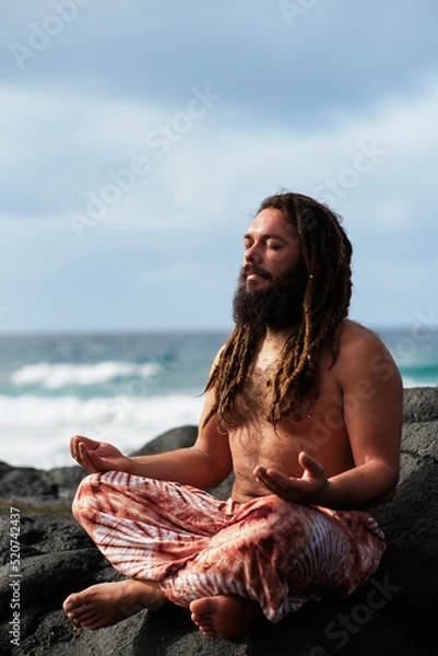 Fototapeta vertical photo, rasta boy with beard meditating by the sea