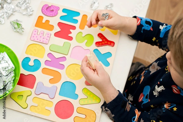 Obraz Two year boy playing with wooden alphabet letters board. Letters wrapped in foil. Intellectual game, preschool implement for early education. Verbal and memory training exercise.