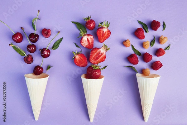 Fototapeta Splash of summer berries from ice cream cones on purple background. Summer time food flat lay