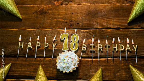 Fototapeta golden letters of the candle with the number happy birthday, the background of the pie with candles happy birthday on the background of brown stranded boards. Postcard Happy birthday 78